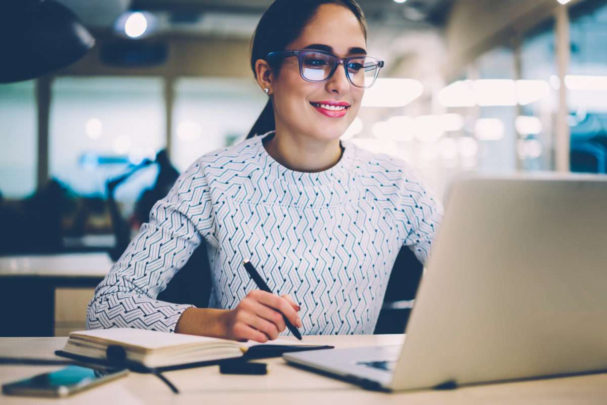 une femme prend des notes devant son ordinateur